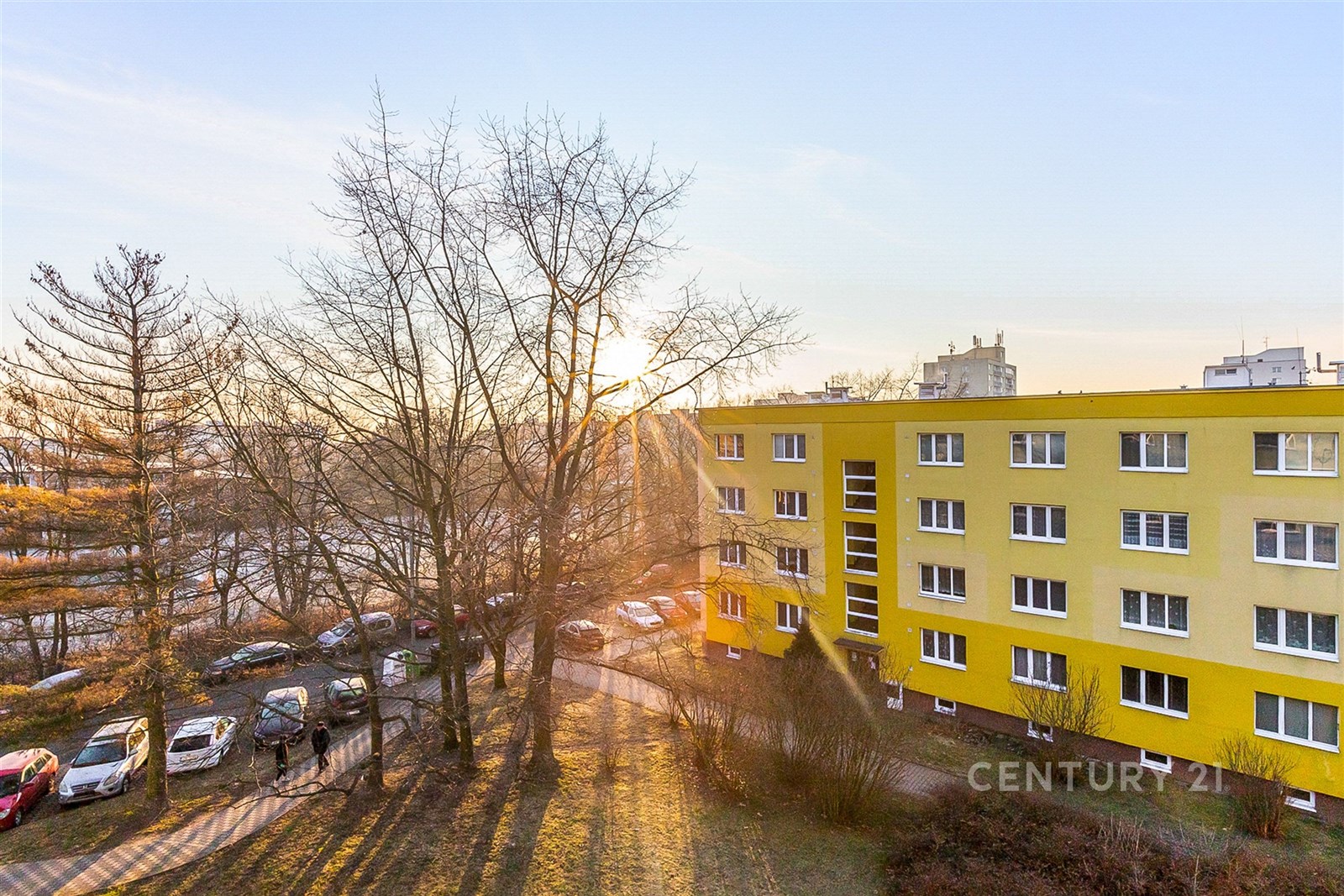 Žlutý panelový dům s velkými okny, okolní zeleň, k