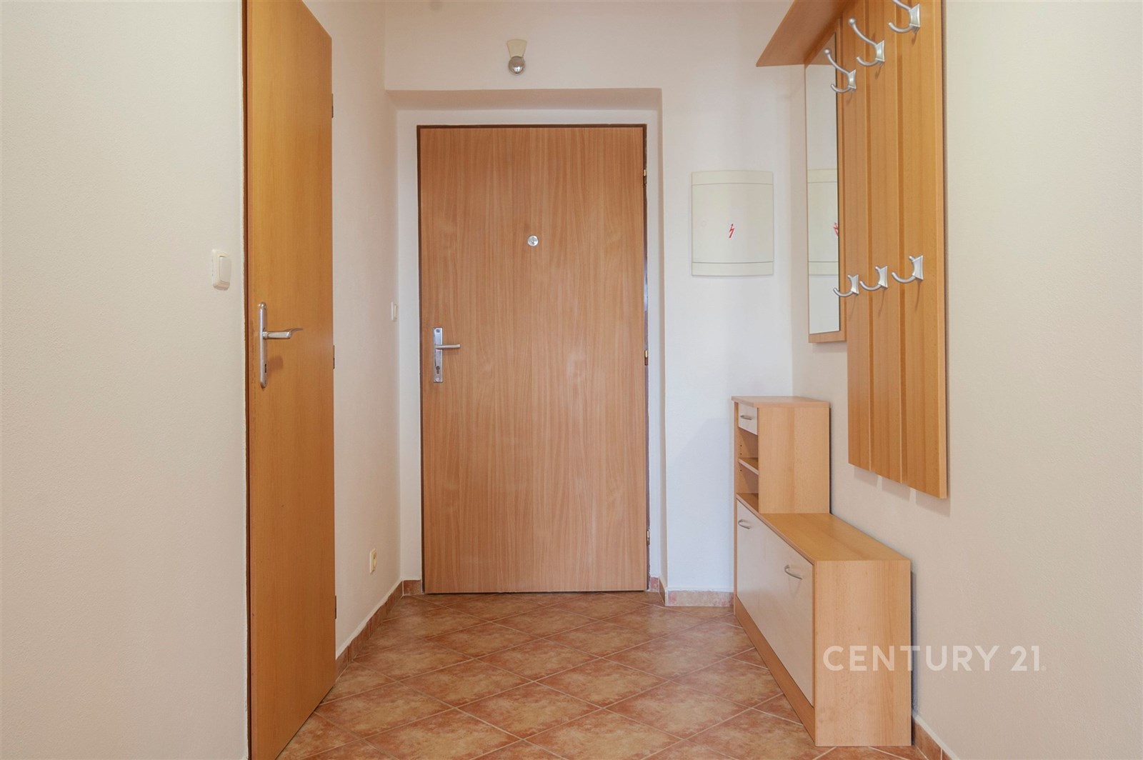 Předsíň s dlažbou, světlá stěna a dřevěný nábytek. Vestavěná skříň poskytuje úložný prostor, moderní a praktické uspořádání.