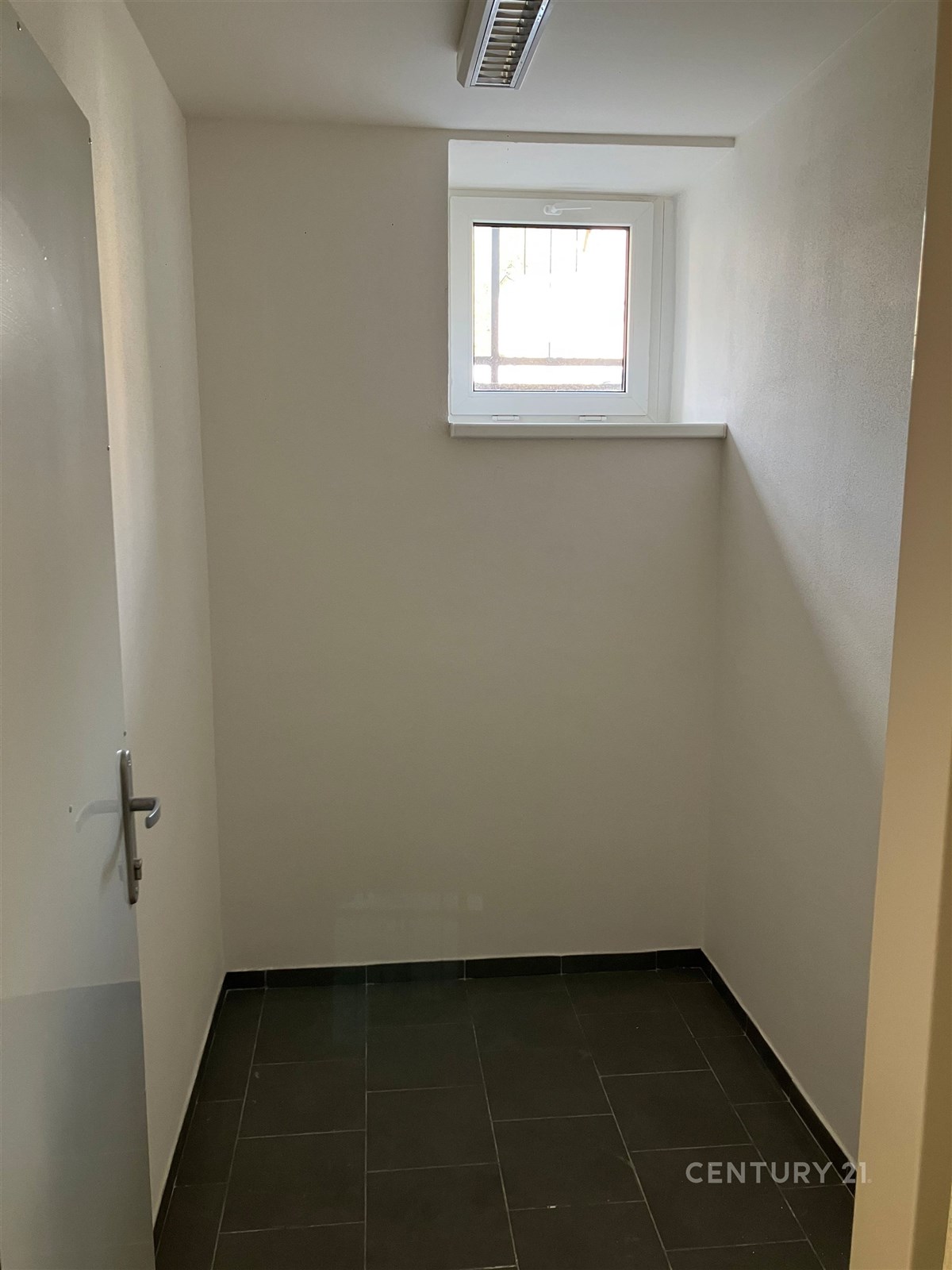 Malý suterénní pokoj s dlažbou a malým oknem. Jednoduchý design, ideální jako úložný prostor nebo prádelna.