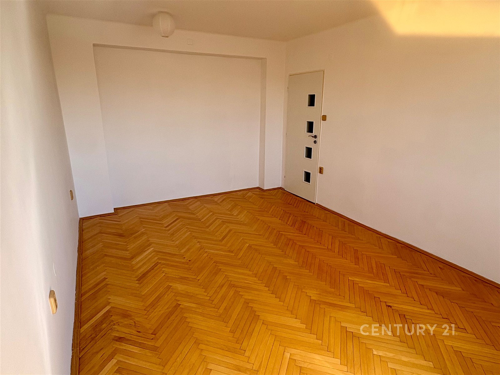 Světlý obývací pokoj s parketovou podlahou, čisté bílé stěny, moderní osvětlení, minimalistický design, připravený k nastěhování.