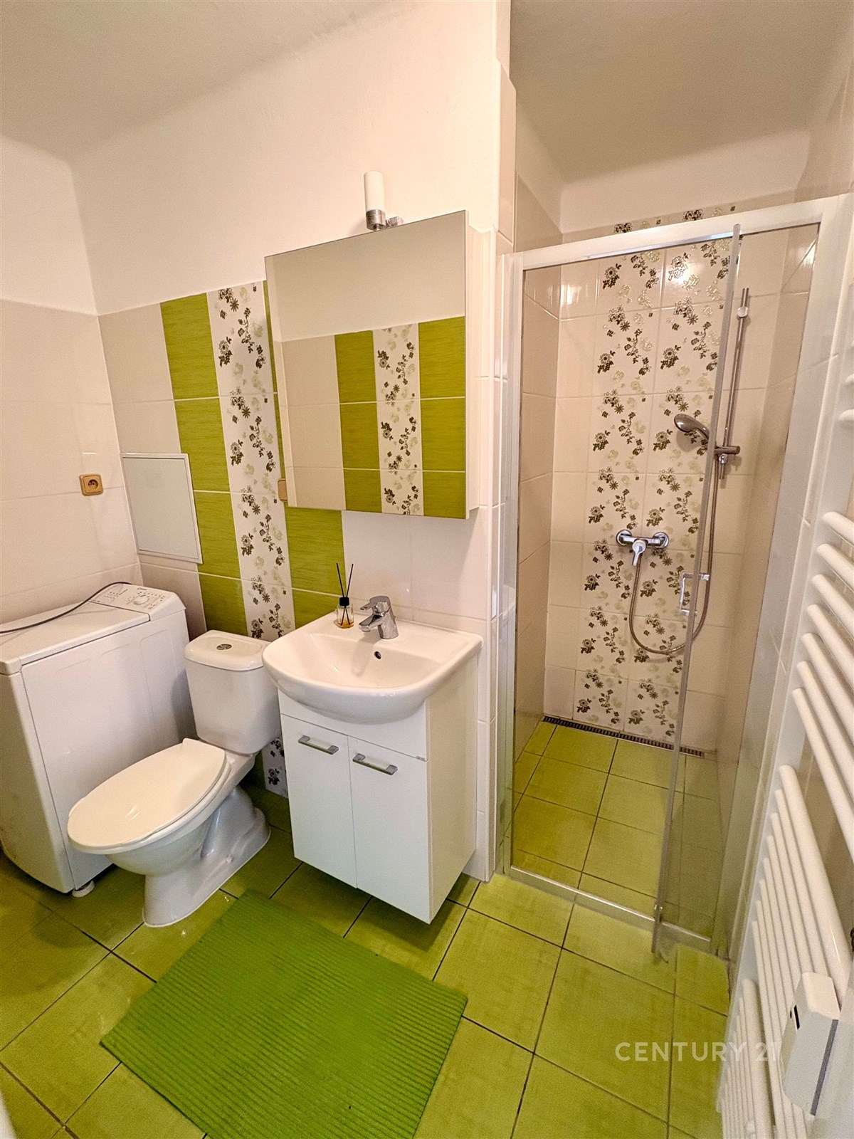 Moderní koupelna s dlažbou a sprchovým koutem, výrazné zelené akcenty, pračka, svěží stylový design.