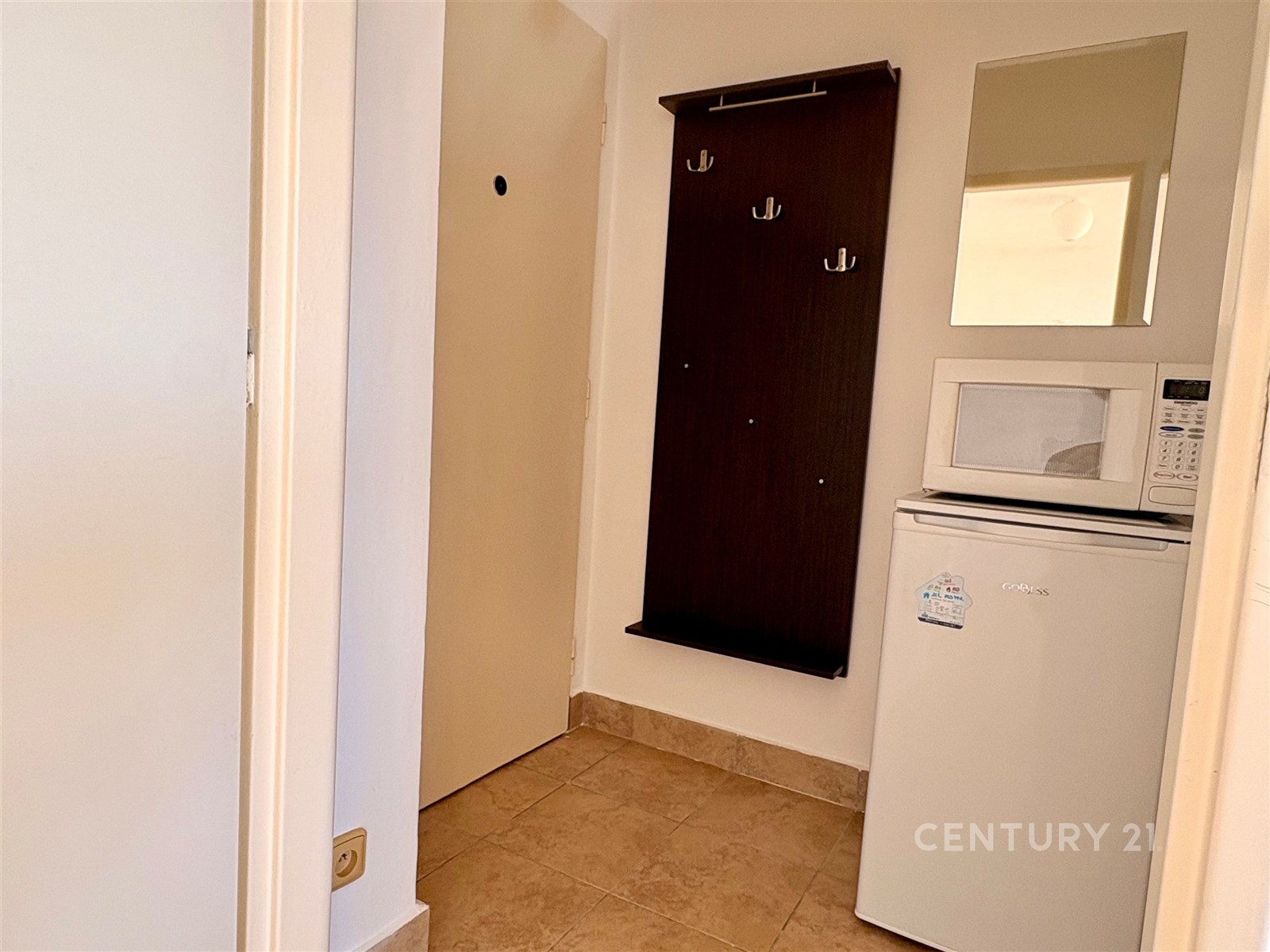 Chodba s dlažbou zahrnuje malou lednici a mikrovlnnou troubu, tmavé věšáky na oblečení, moderní a praktické řešení pro úložný prostor.