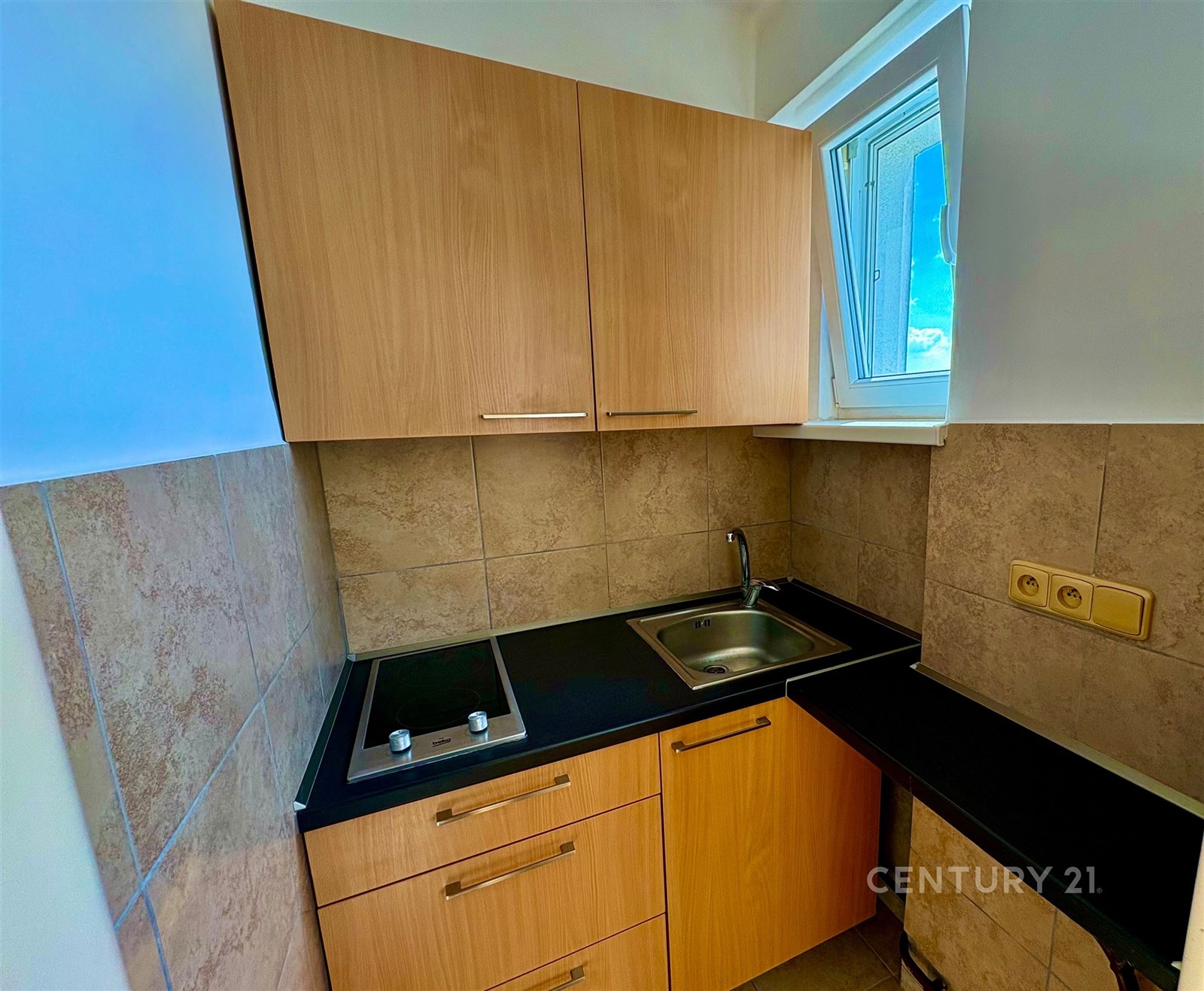 Malá kuchyň s dřevěnými skříňkami a dlažbou na stěnách, vestavěná varná deska, okno propouštějící přirozené světlo mavkjoddfvkdjq 