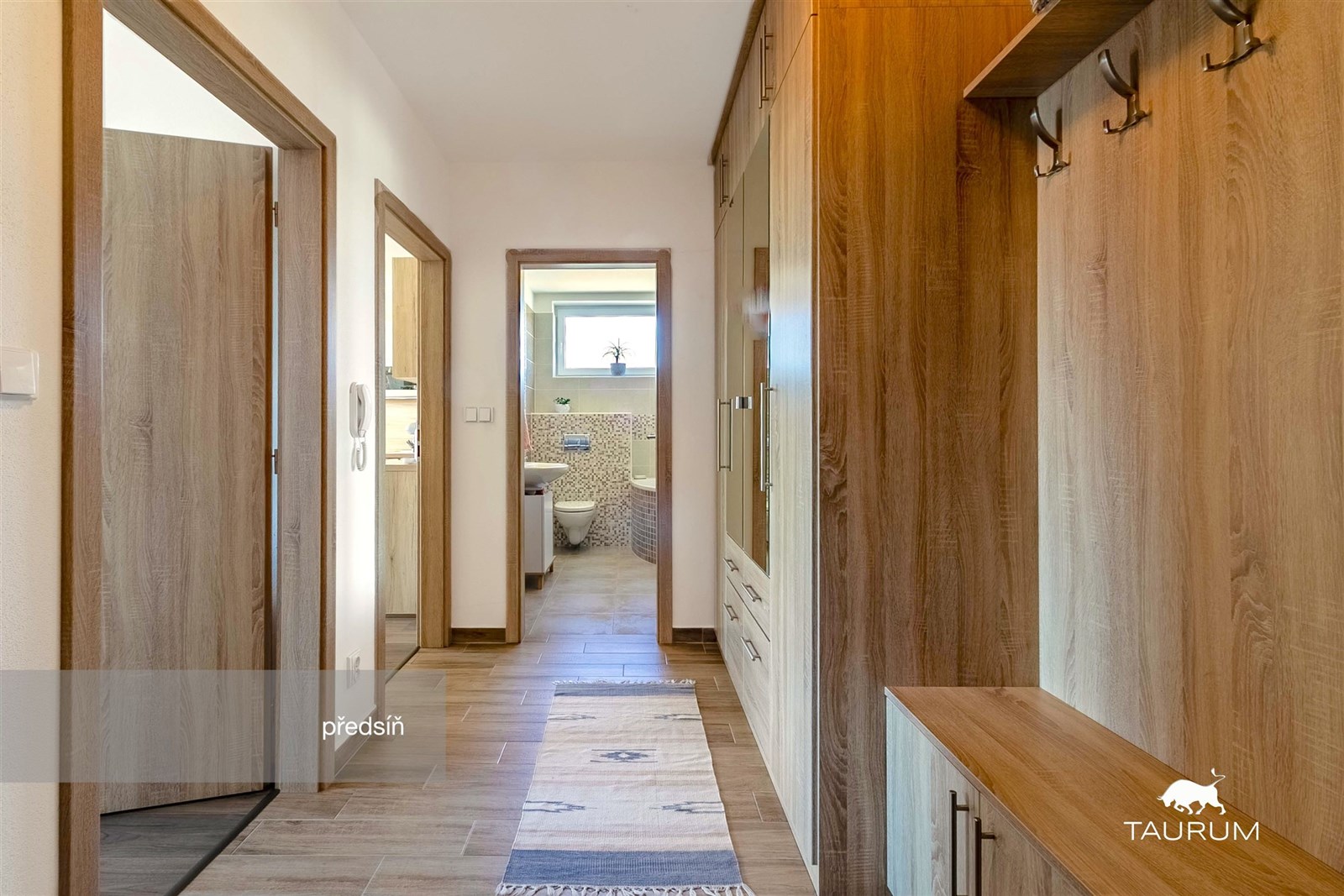 Předsíň s vestavěnými skříněmi, dřevěnými prvky a dlažbou, nabízí moderní a praktický prostor.