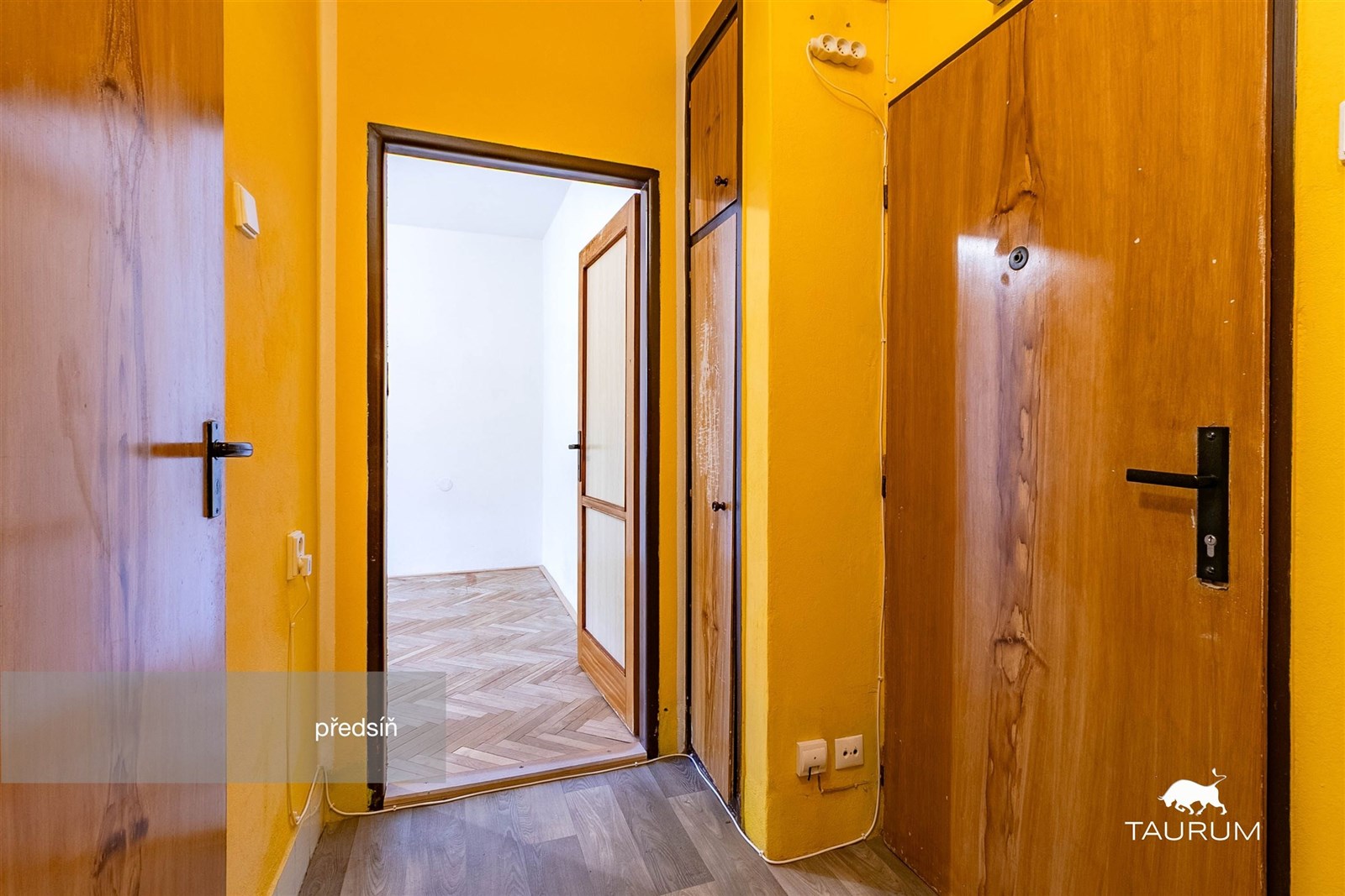 Úzká předsíň s dlažbou a dřevěnými dveřmi vede do 