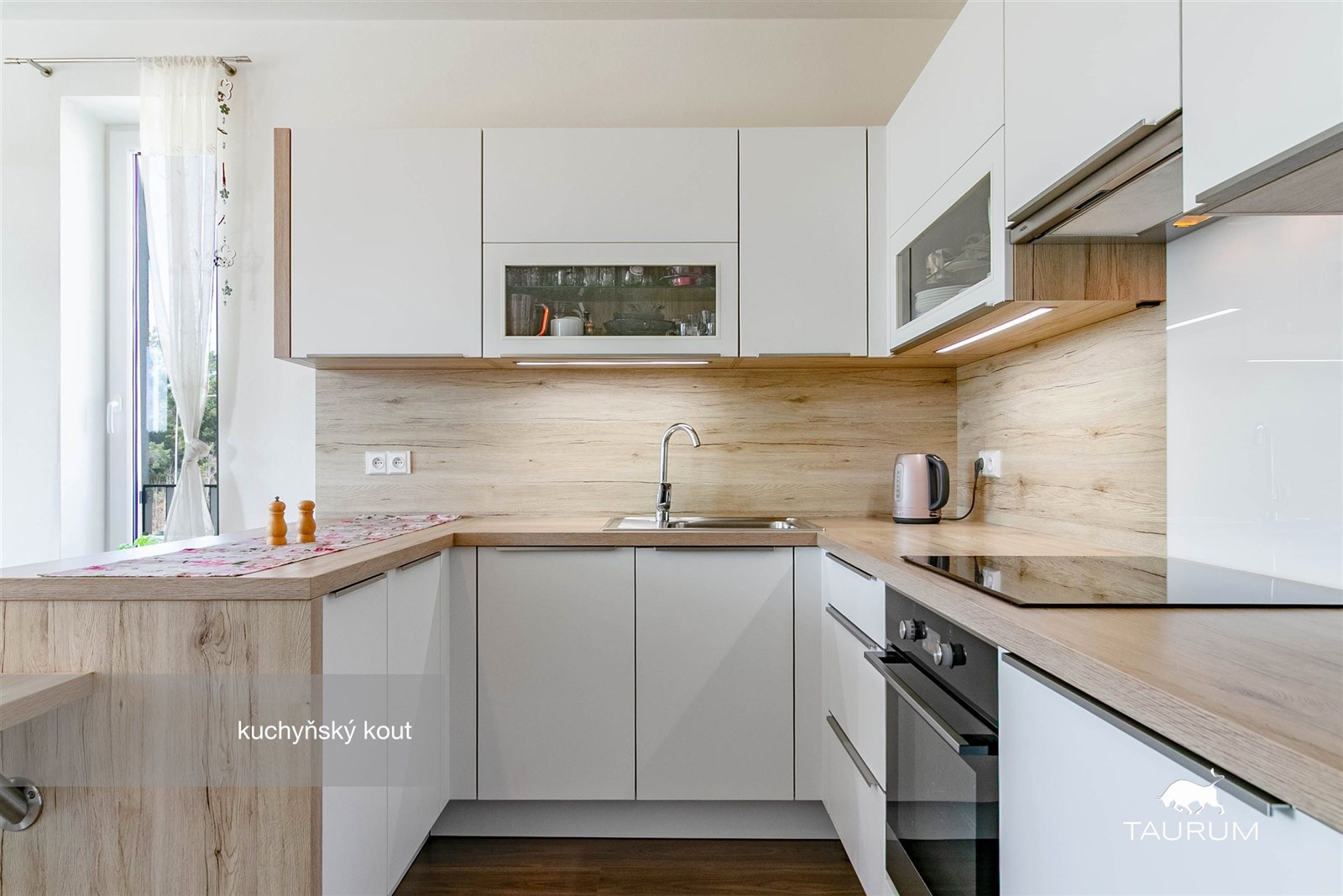 Moderní kuchyňský kout s dřevěným obložením, vestavěnými spotřebiči a parketovou podlahou nabízí světlý a elegantní prostor.