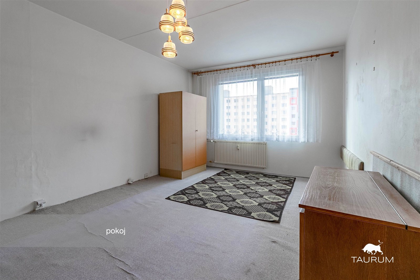 Světlý pokoj s velkými okny, kobercovou podlahou a vestavěnými skříněmi, ideální pro rekonstrukci.