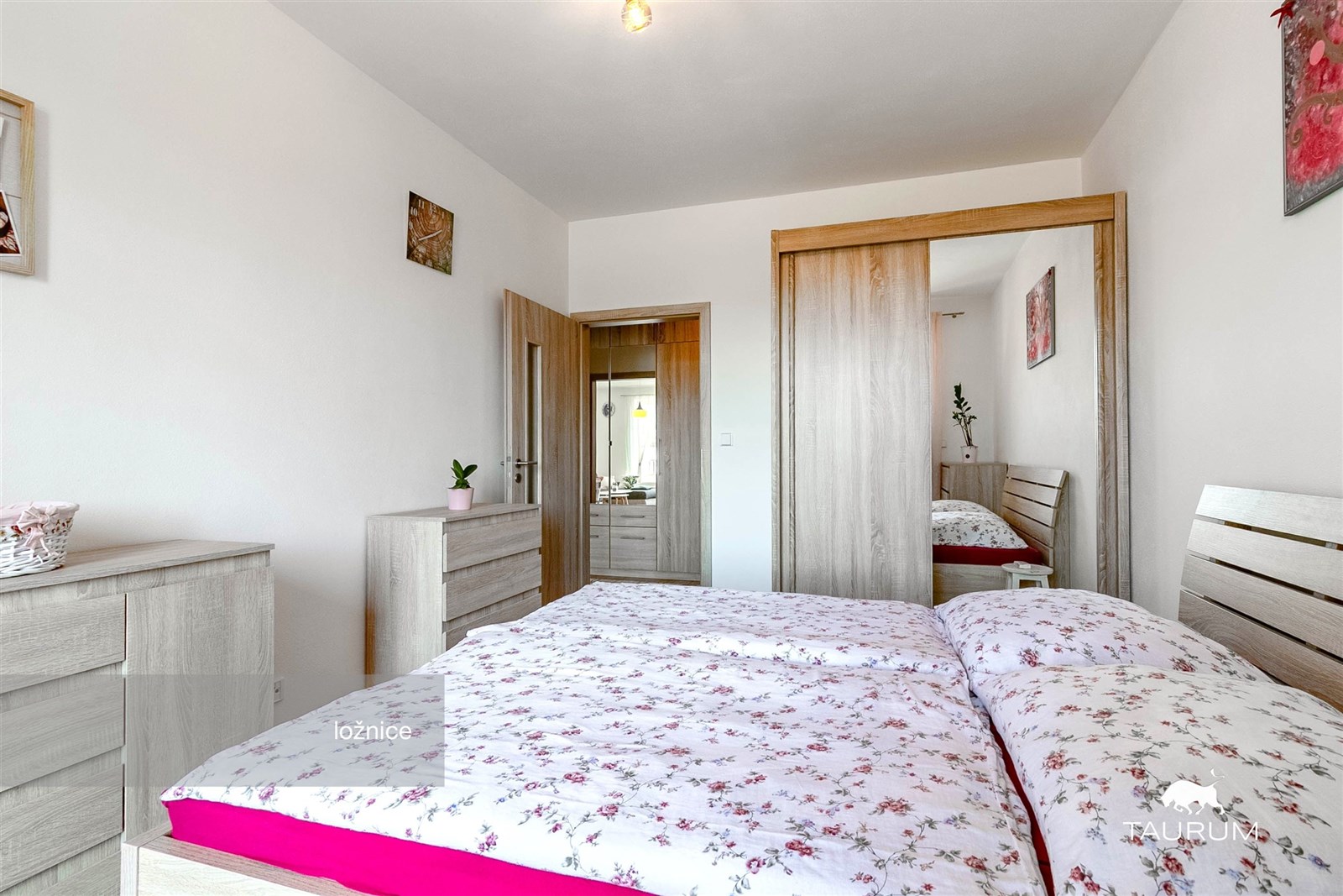 Prostorná ložnice s moderní vestavěnou skříní, parketová podlaha, světlé stěny, elegantní dřevěný nábytek.