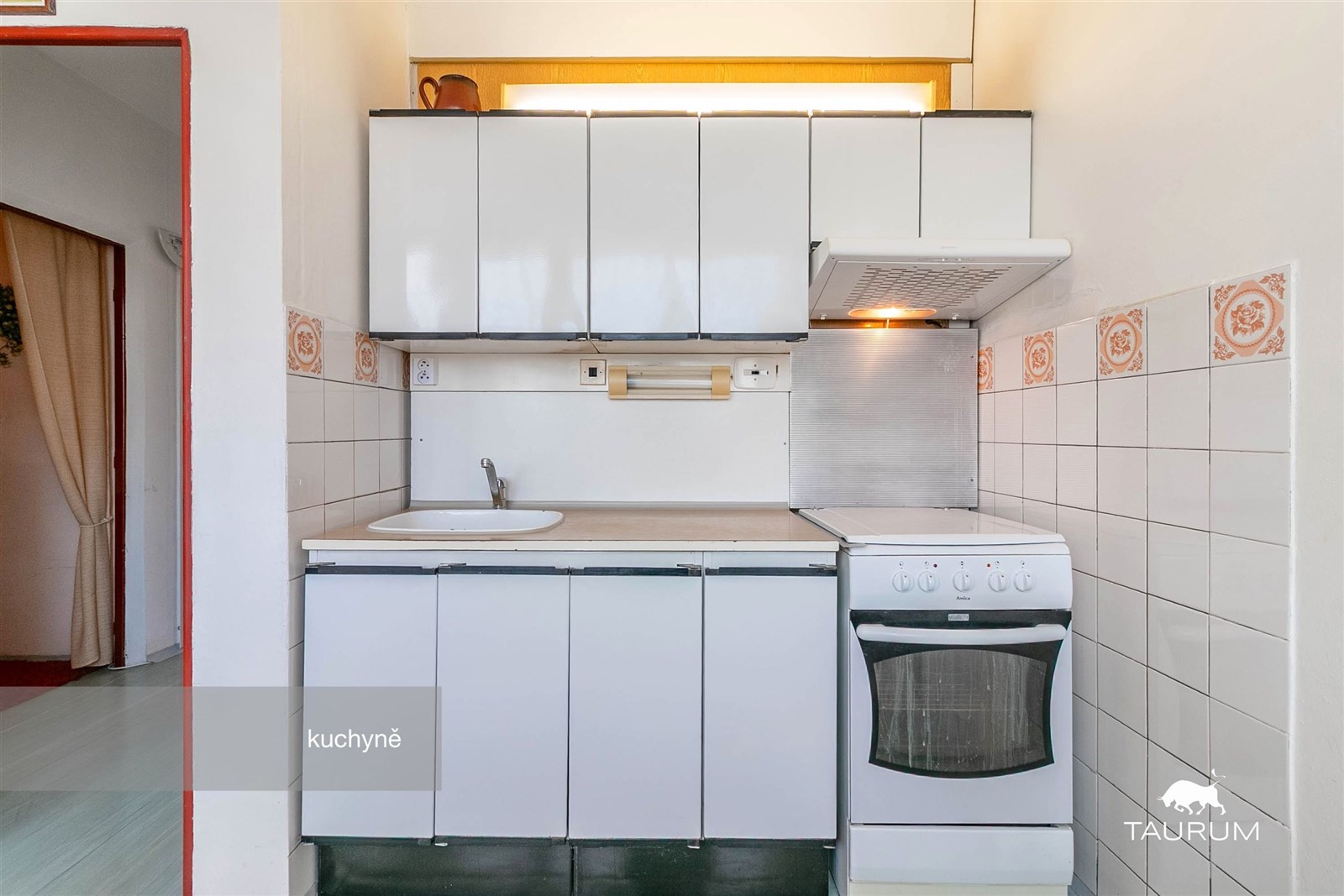 Malá kuchyň s bílými skříňkami, dlažbou a plynovým sporákem v udržovaném stavu