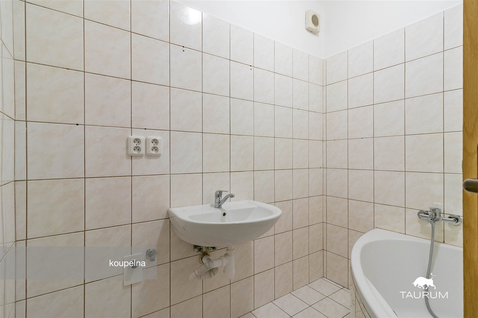 Koupelna s dlažbou, bílými obklady a umyvadlem. Sv