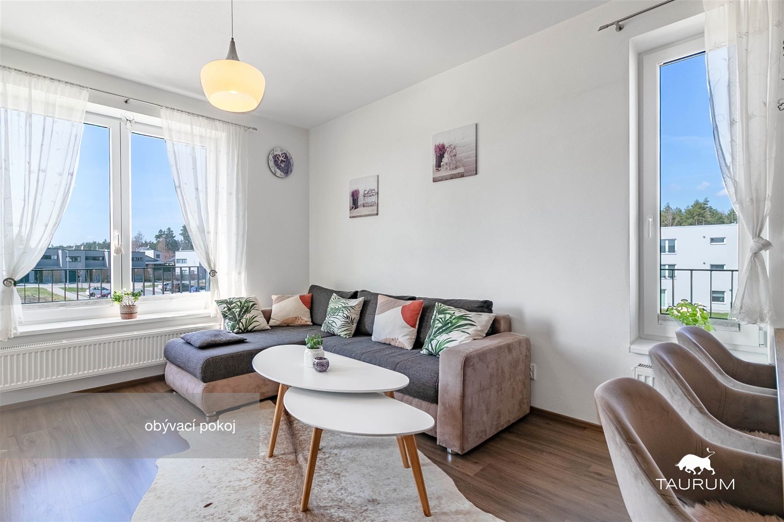 Světlý obývací pokoj s velkými okny, moderní výzdobou a dřevěnou podlahou, která dotváří elegantní atmosféru.