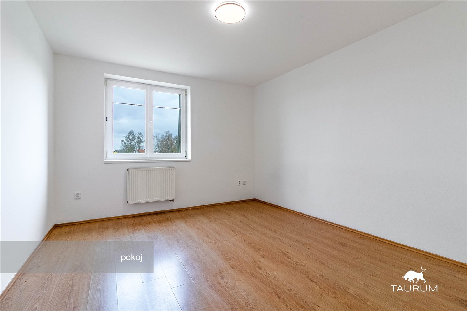 Světlý pokoj s parketovou podlahou, velkým oknem a