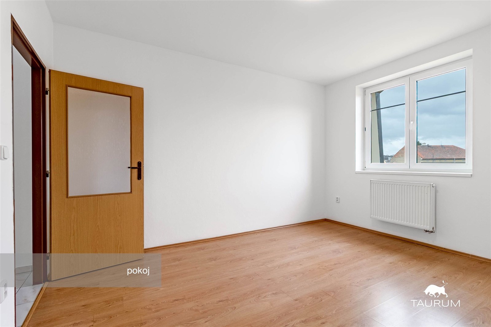 Světlý pokoj s parketovou podlahou a velkými okny,