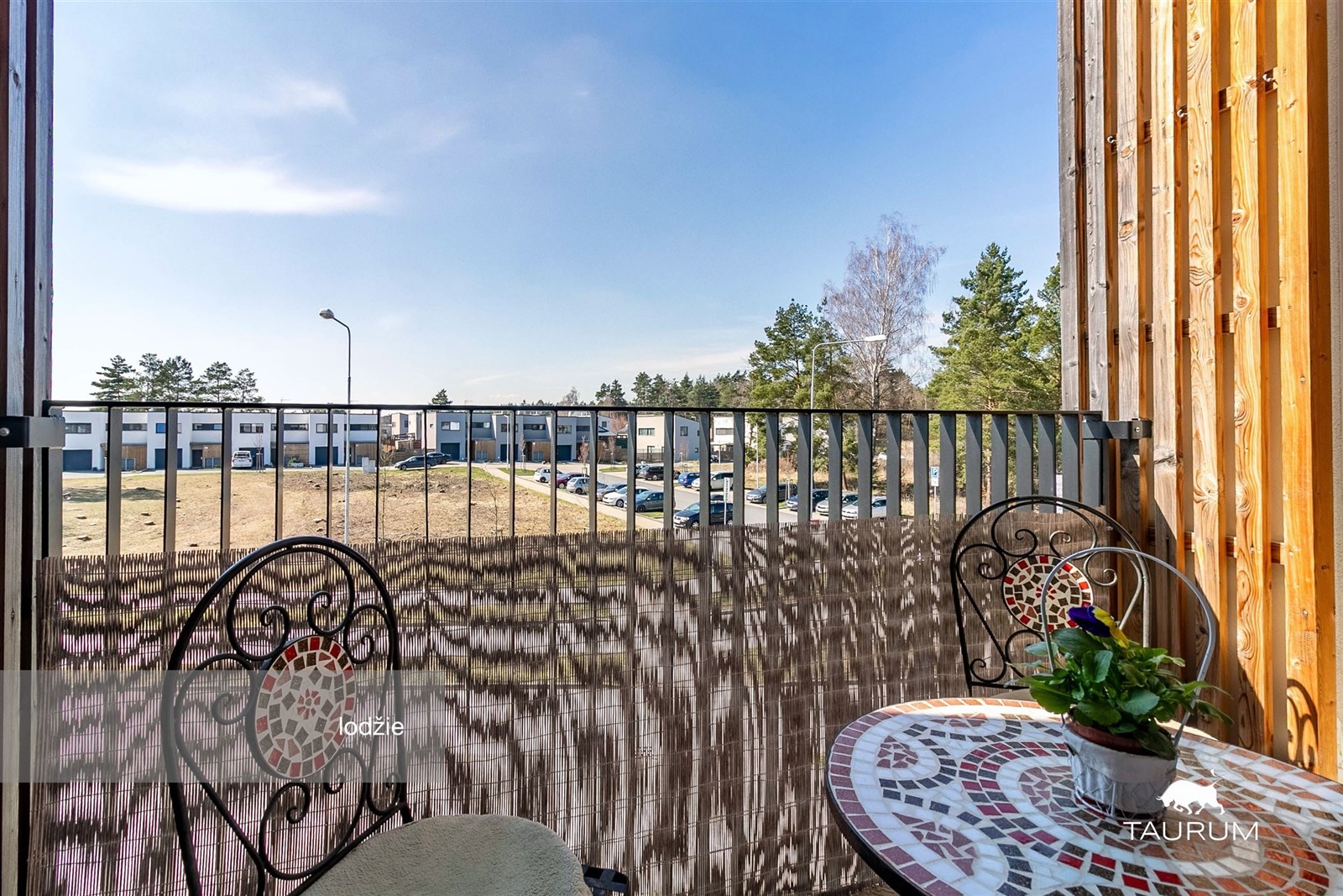 Balkón s kovovým zábradlím nabízí prostor k relaxaci, s keramickým stolkem a výhledem na klidnou lokalitu. Kombinace dřeva a kovu přidává moderní nádech.