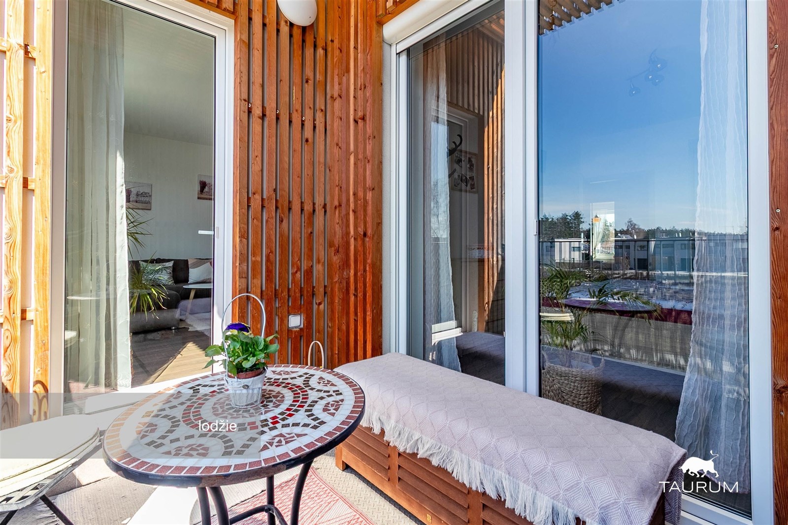 Balkón s moderním designem, dřevěným obložením a velkými okny nabízí relaxační prostor s výhledem. Ideální pro relaxaci a odpočinek.