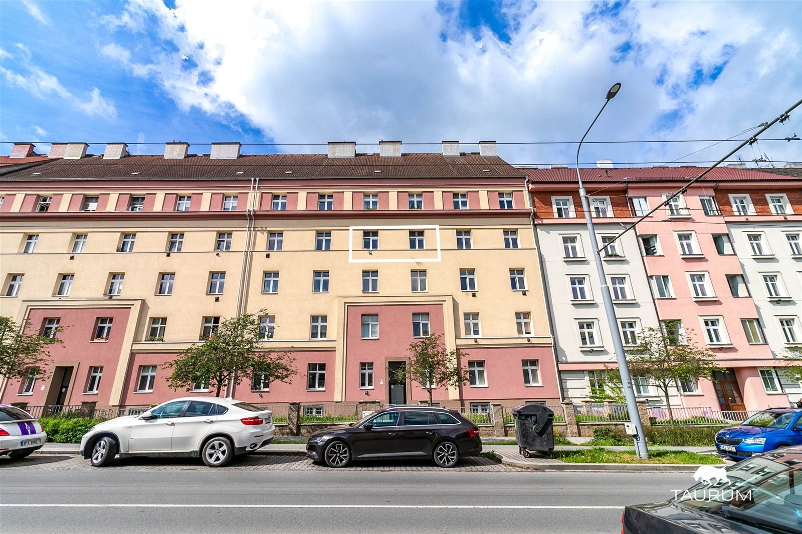 Vícepatrový obytný dům s barevnou fasádou, velkými okny, parkováním před budovou, nacházející se ve městě.