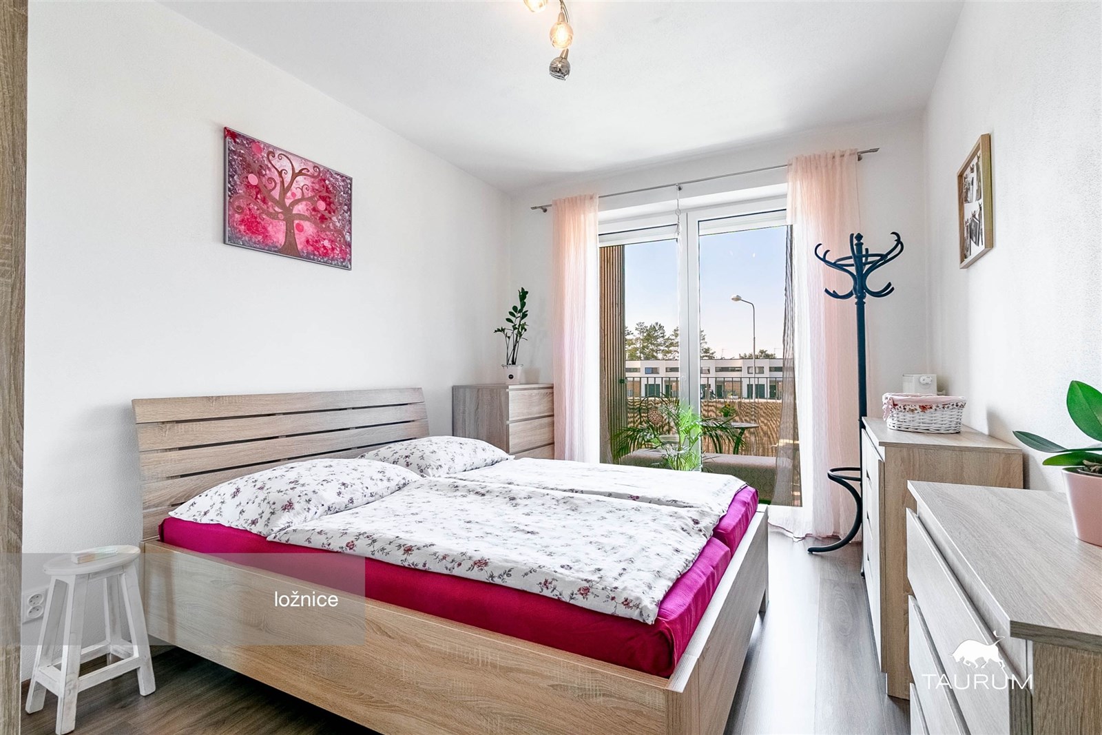 Světlá ložnice s dřevěným nábytkem, velkými okny a moderním designem. Laminátová podlaha dodává prostoru elegantní vzhled.