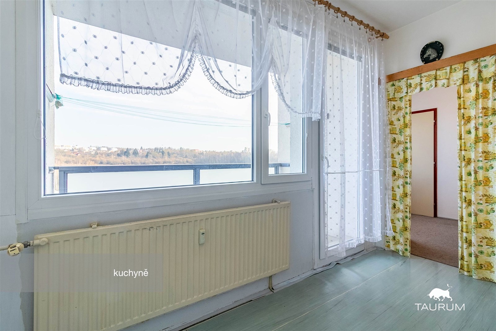 Světlá kuchyň s velkými okny, PVC podlahou a záclonami, která poskytuje krásný výhled na okolní krajinu, ideální pro moderní bydlení.