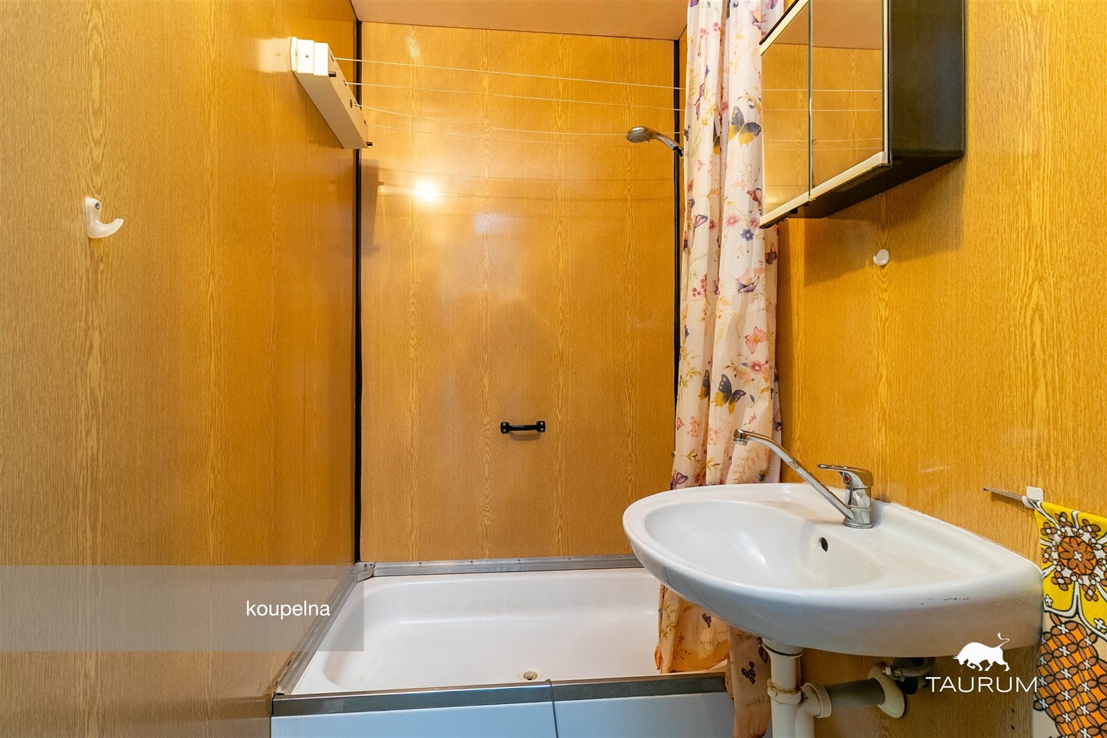 Kompaktní koupelna s dřevěným obložením, vanou a umyvadlem. Dřevo přináší teplo a rustikální styl, prostor je funkční a útulný.