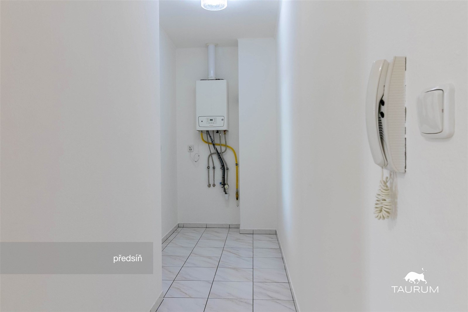 Úzká předsíň s dlažbou, světlá stěna a ohřívač vod