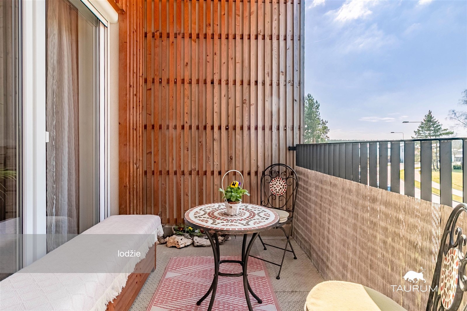 Krytá lodžie s dřevěným obložením, stylovým nábytkem a výhledem, nabízí komfortní prostor pro relaxaci, podlahová dlažba a dostatek světla.