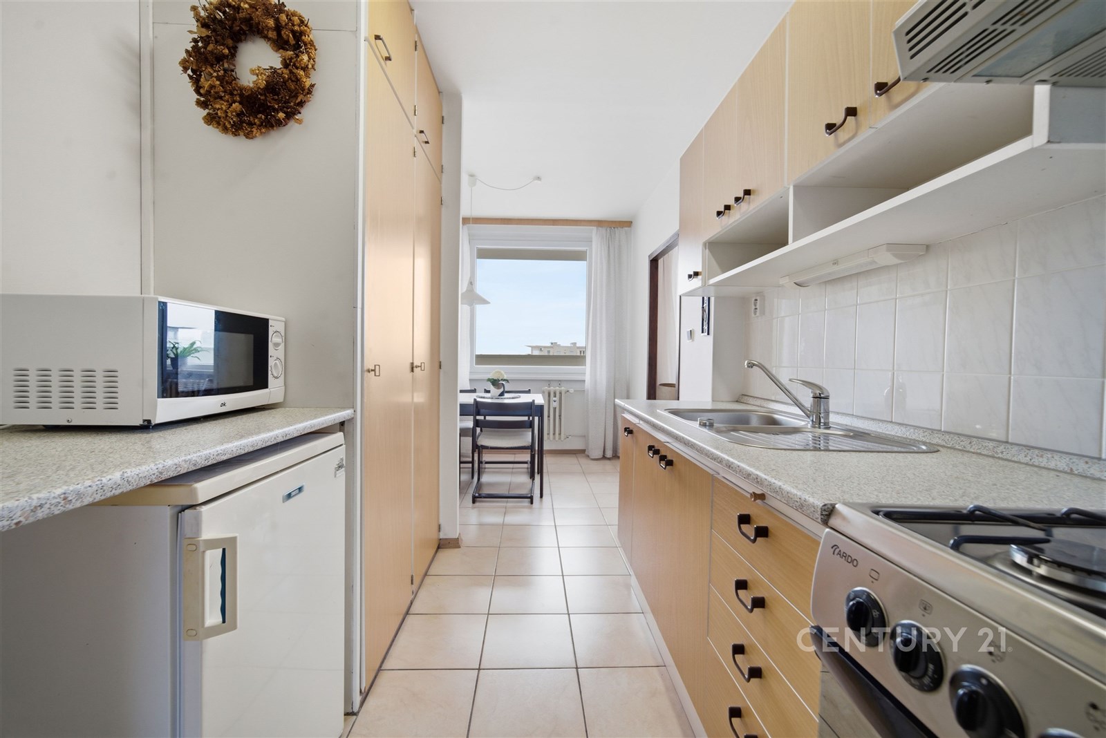 Kompaktní kuchyň s dlažbou, světlými skříňkami a s