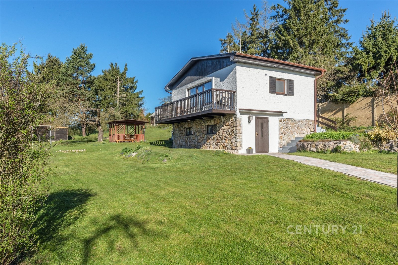 Rodinný dům s kamenným soklem a dřevěným balkónem, nacházející se na prostorném trávníku na okraji lesa, skvělý pro milovníky přírody.