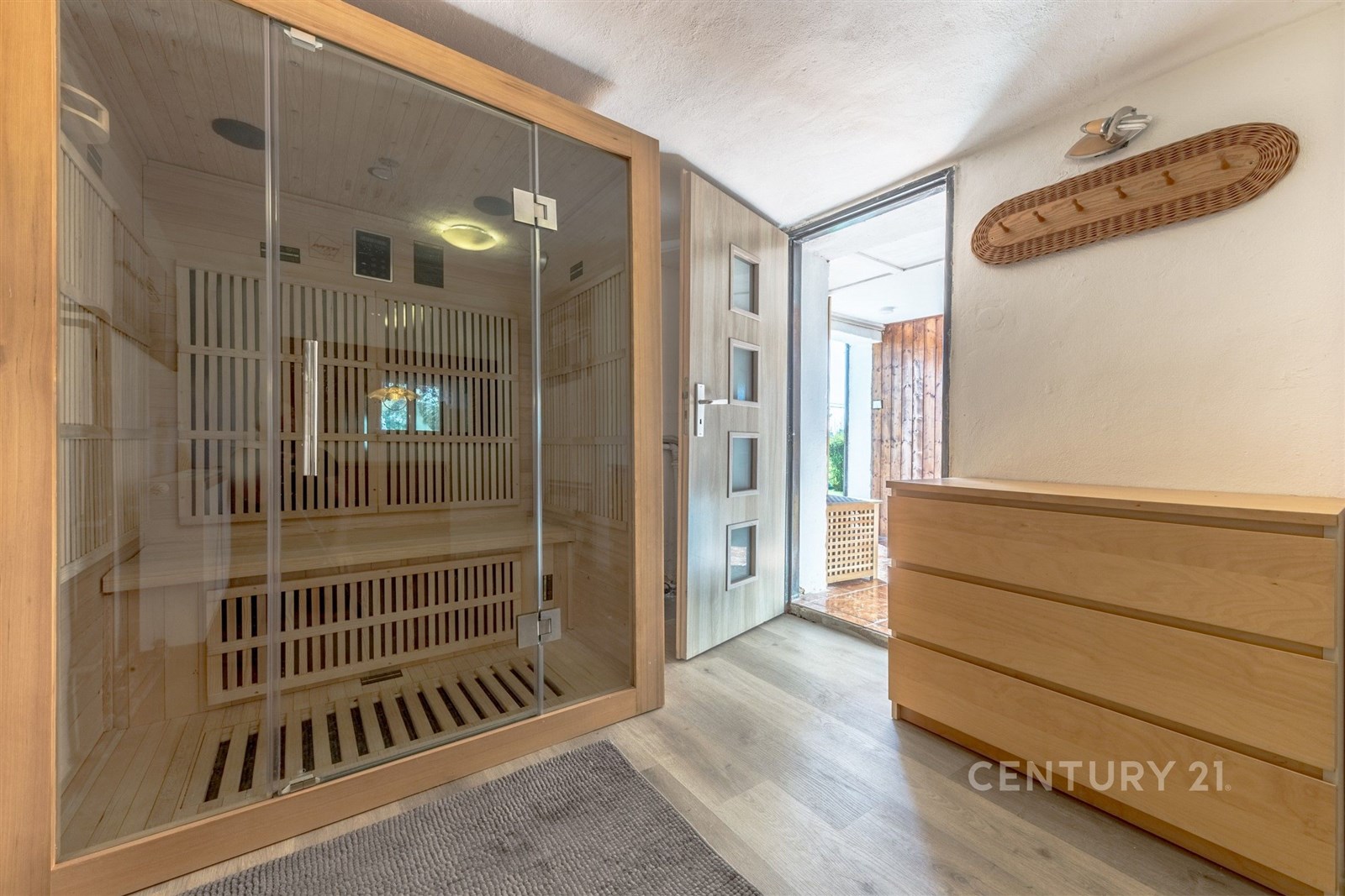 Domácí sauna s prosklenými dveřmi, dřevěné obložení a světlé parketové podlahy, nabízí moderní relaxační prostor s přístupem na terasu.