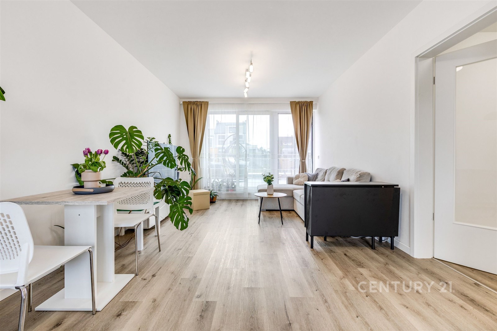Světlý obývací pokoj s moderní parketovou podlahou, velká okna s výhledem, minimalistický styl s rostlinami a neutrálním nábytkem.
