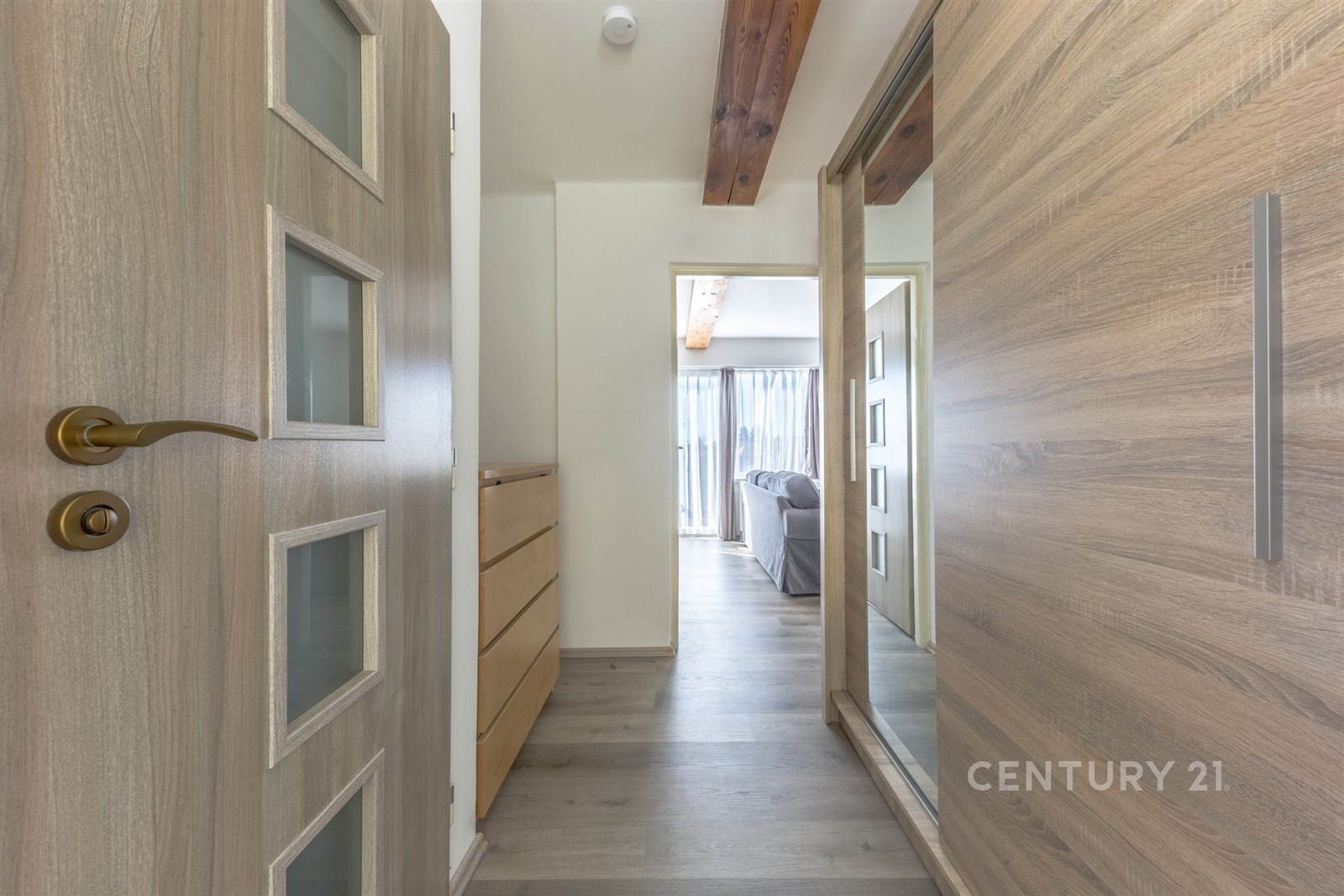 Úzká chodba s dřevěnými dveřmi a vestavěnými skříněmi, světlý interiér, parketová podlaha, moderní design, velká okna v obývacím pokoji.