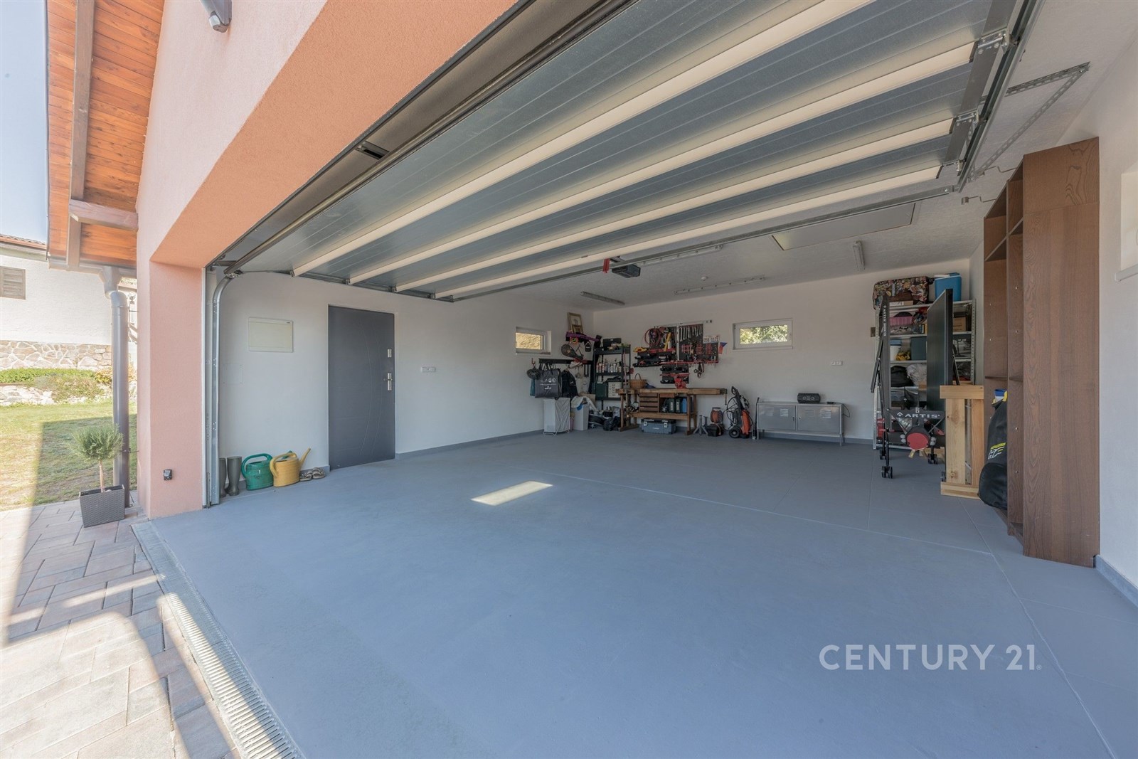 Prostorná garáž s betonovou podlahou, dílenským koutkem a vestavěnými policemi, ideální pro moderní uspořádání a úložný prostor.