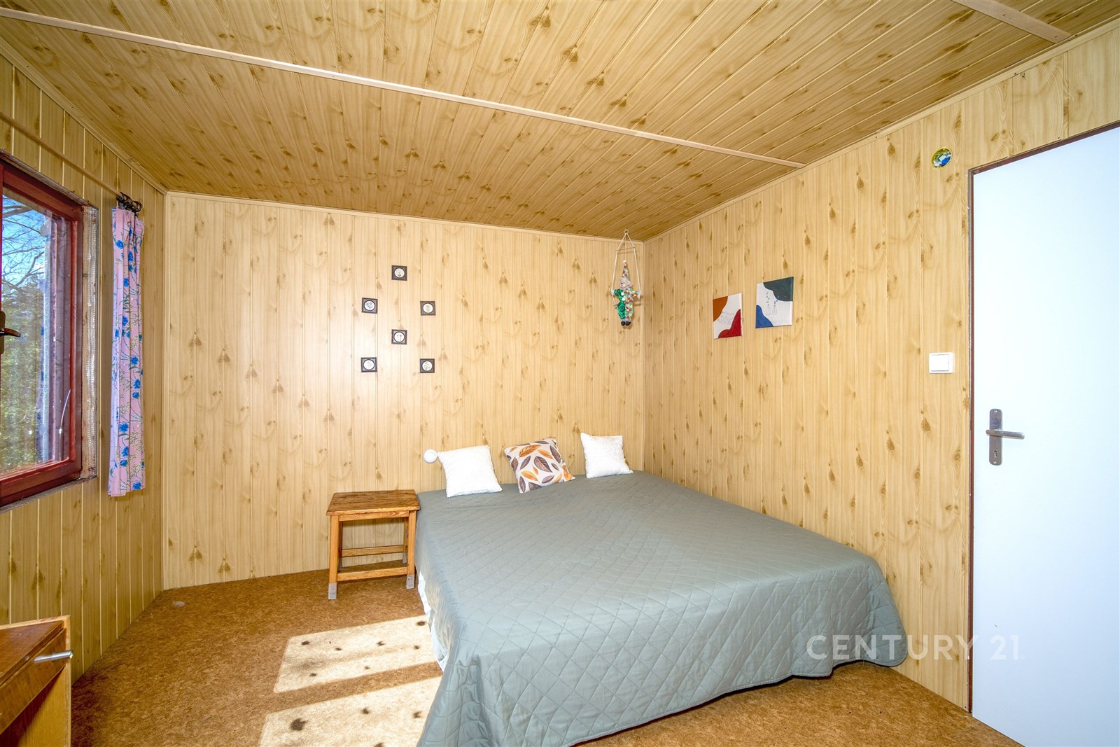 Ložnice s dřevěným obložením, velkými okny a parketovou podlahou nabízí útulný a rustikální styl.