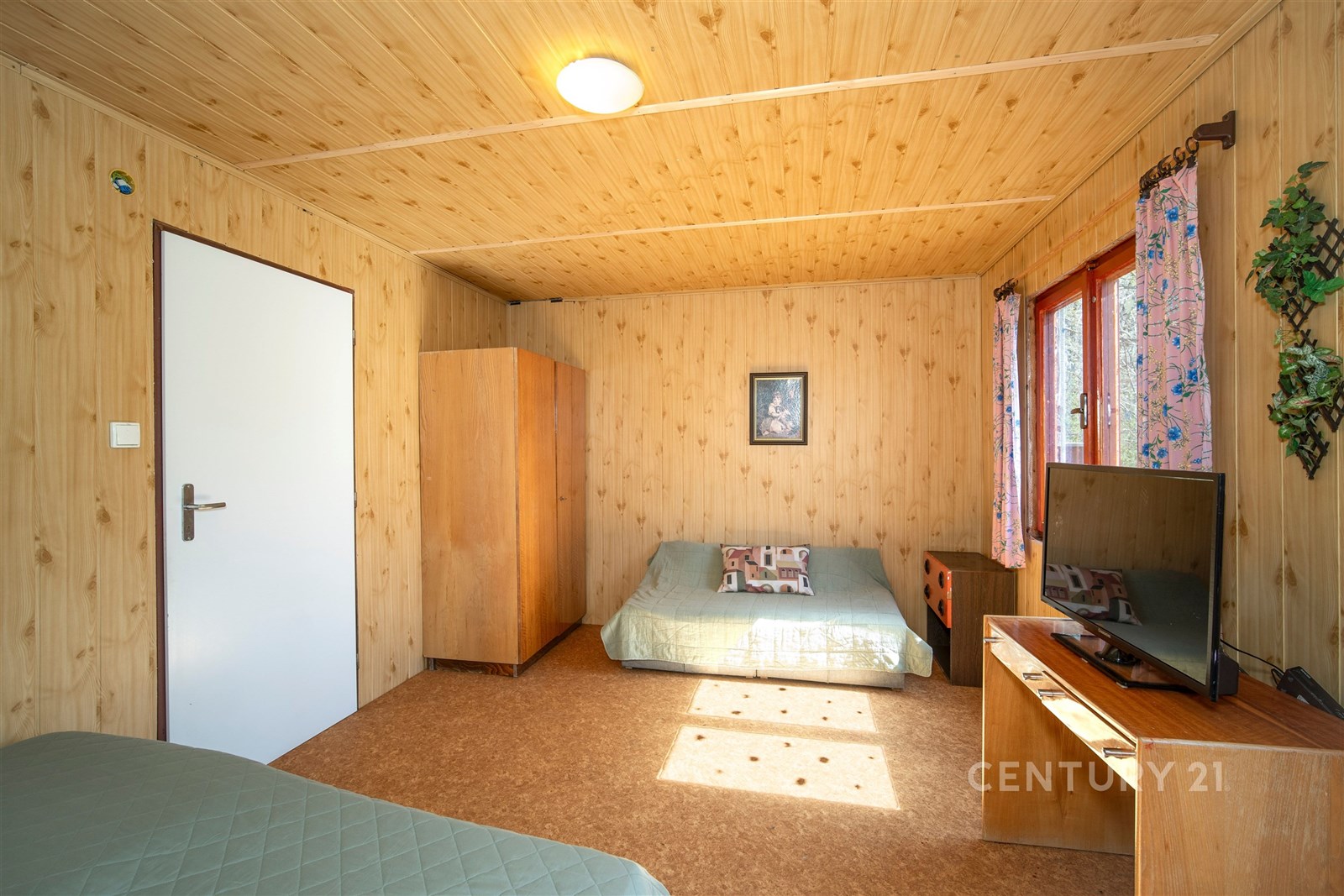 Rekreační pokoj s dřevěným obložením, velkými okny a pohodlným posezením nabízí útulnou atmosféru, ideální pro relaxaci v přírodě.