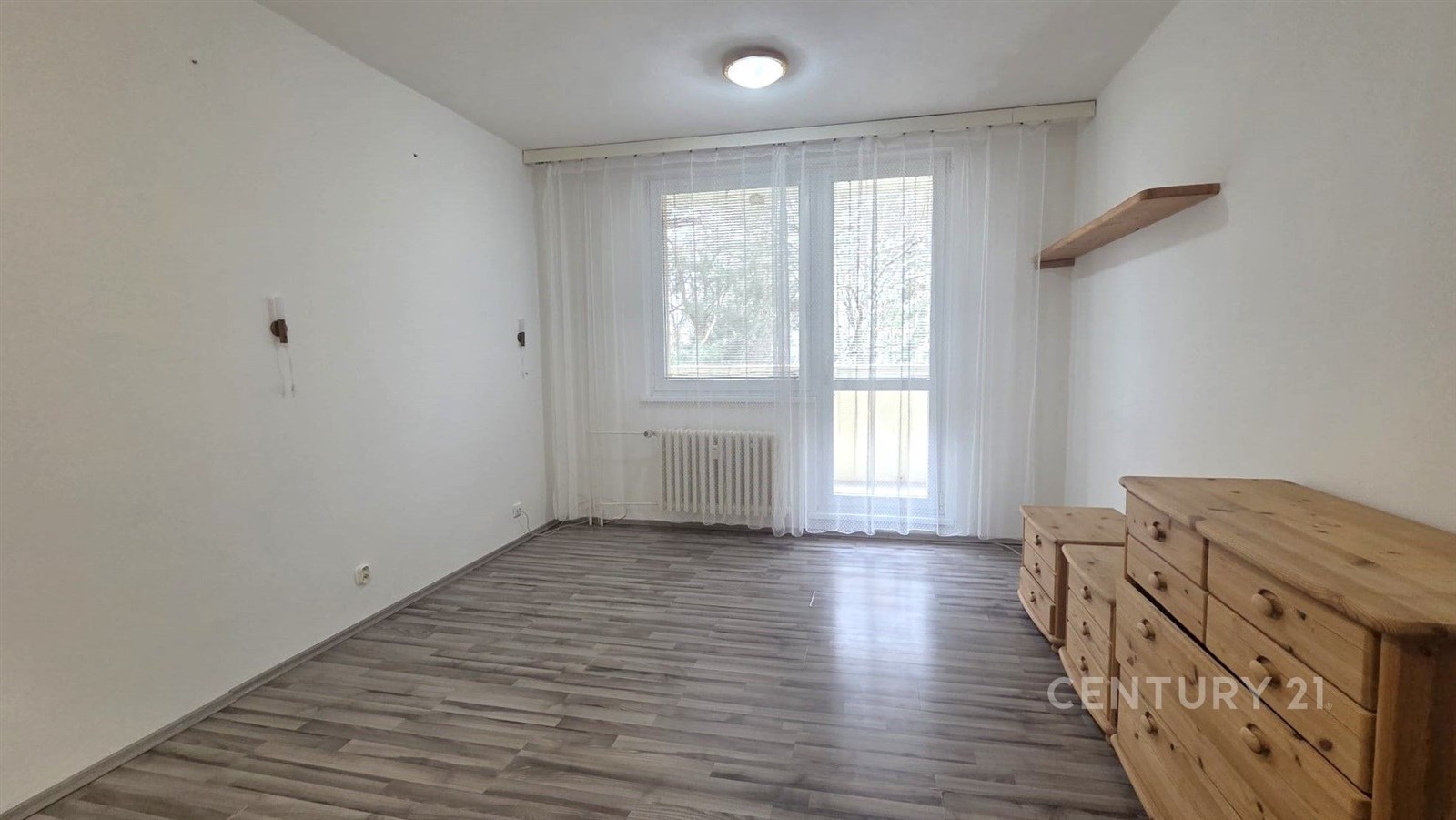 Světlý obývací pokoj s laminátovou podlahou, velká okna s výhledem do zeleně, dřevěný nábytek, moderní provedení.