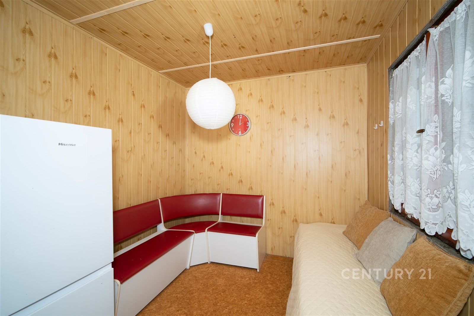 Malý obývací pokoj s dřevěnými obklady, přírodními materiály a jednoduchým stylem, vybavený lavicí a velkým oknem pro přirozené světlo.