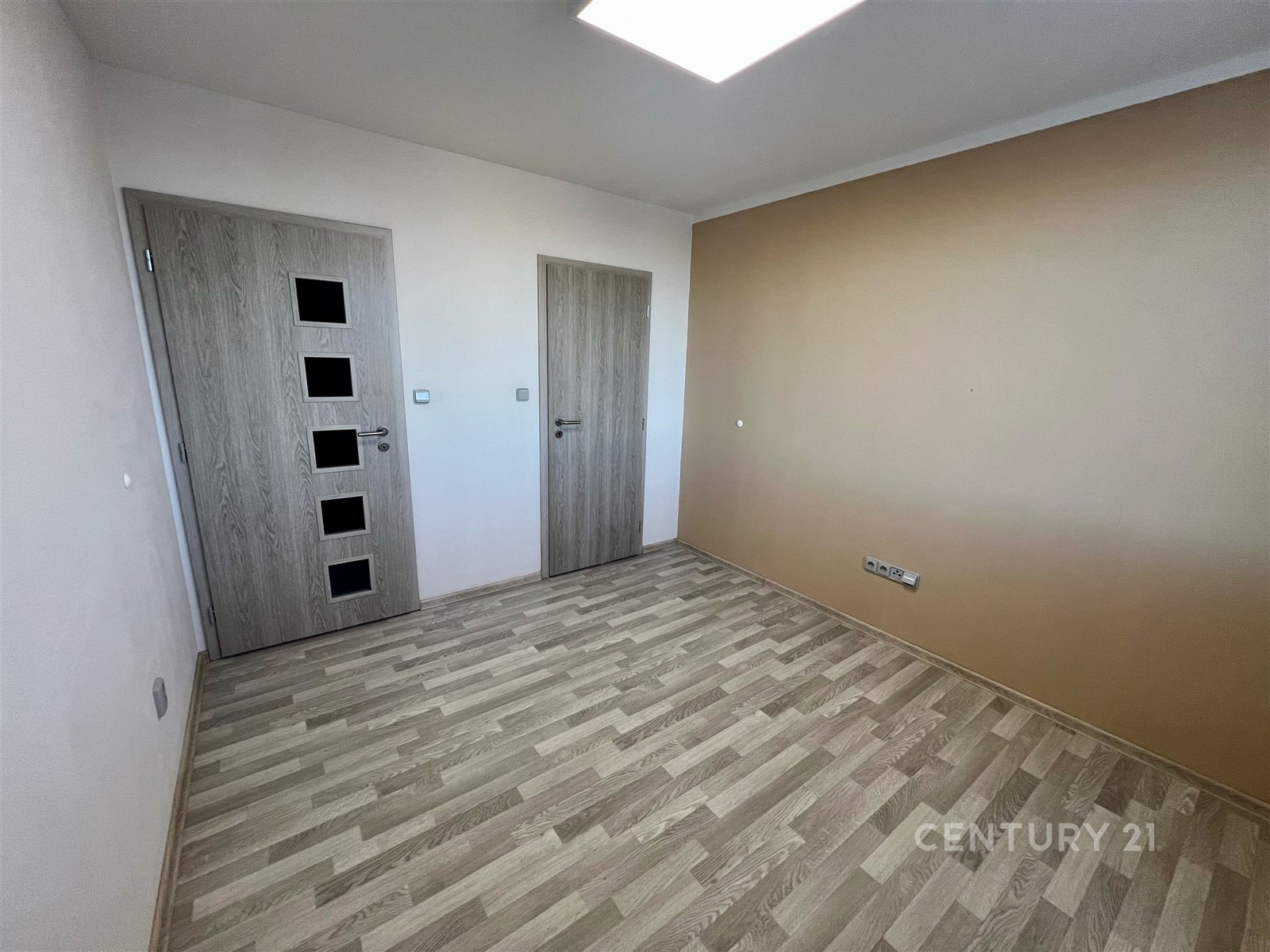 Prázdný pokoj s dřevěnou podlahou, moderními dveřmi a světlými stěnami, ideální pro personalizaci a zařízení dle vlastního vkusu.