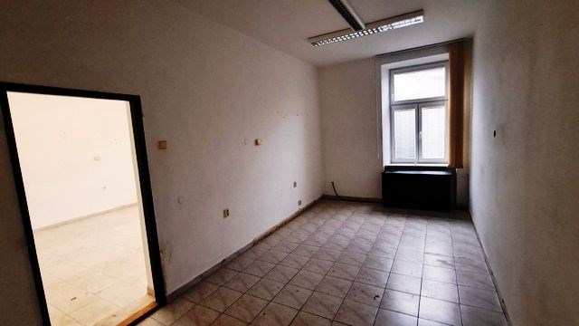 Úzká místnost s dlažbou, velké okno, bílé stěny, d