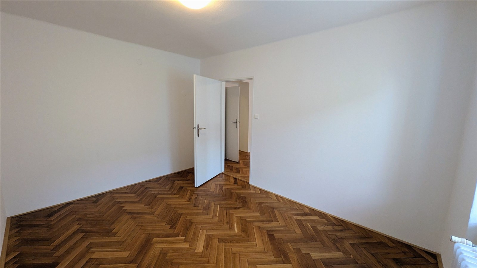 Prázdný pokoj s parketovou podlahou, bílými stěnam