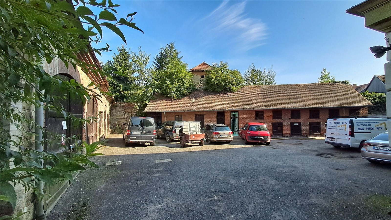 Prázdný dvůr s asfaltovým povrchem pro parkování, obklopený staršími cihlovými stavbami vhodnými pro skladování.