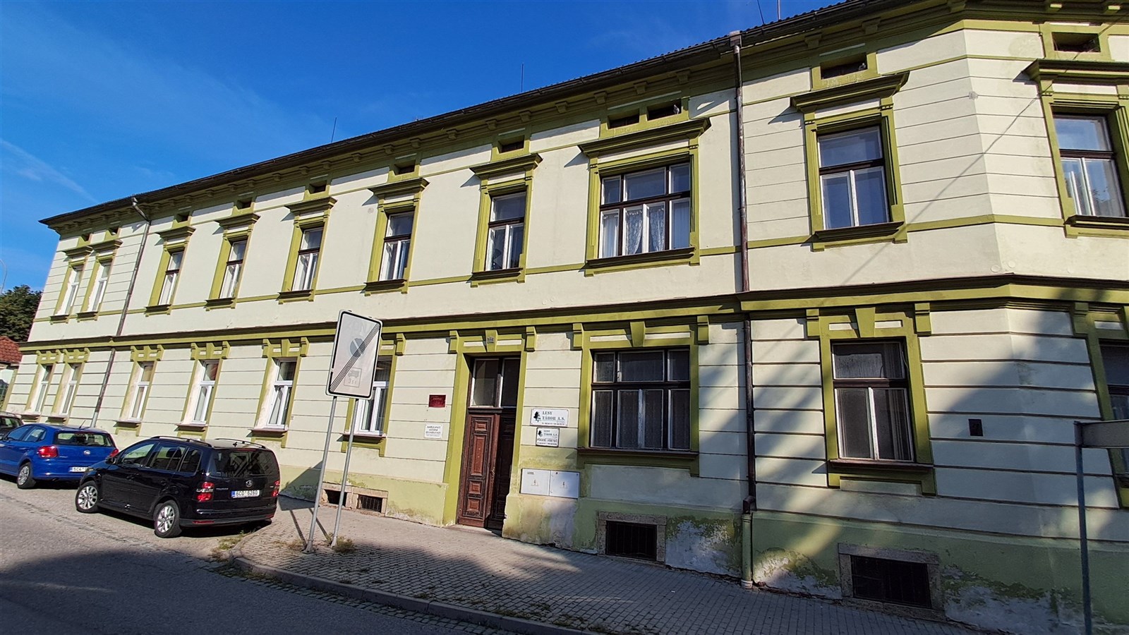 Fasáda historické budovy s klasickými okny a dekorativními prvky ve světlých odstínech, situovaná na klidné ulici v centru města.