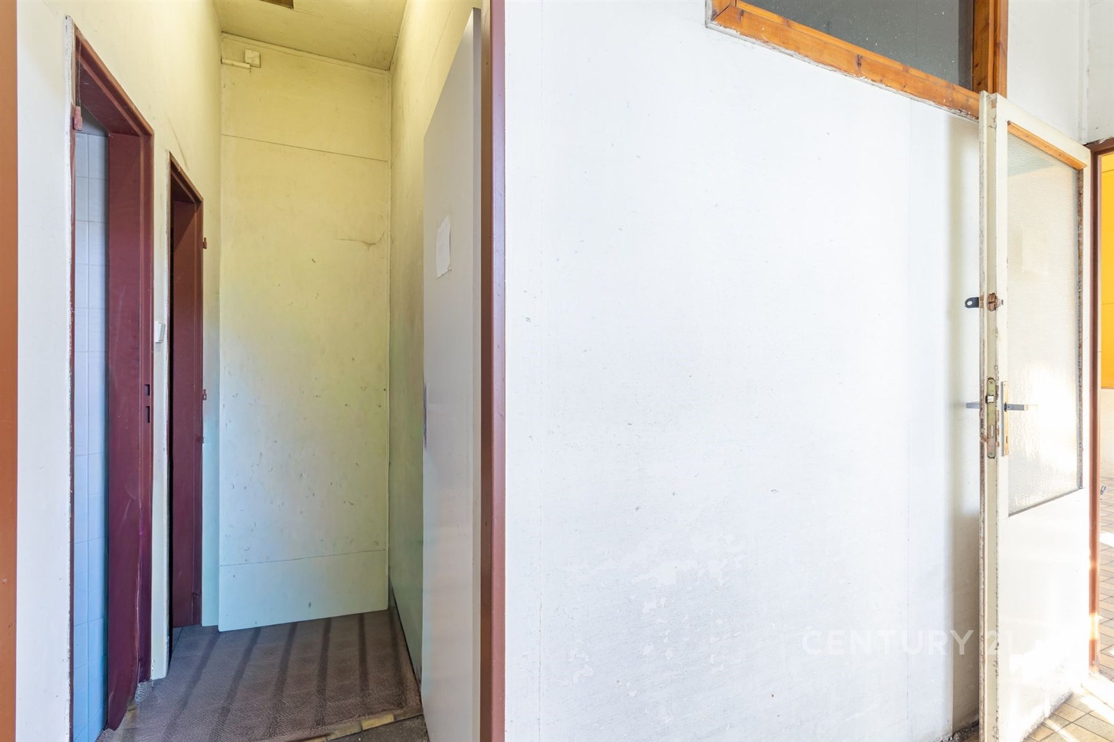 Prázdná chodba s bílými stěnami, kobercovým povrchem a dřevěnými dveřmi, ideální pro renovaci a přizpůsobení osobnímu stylu.