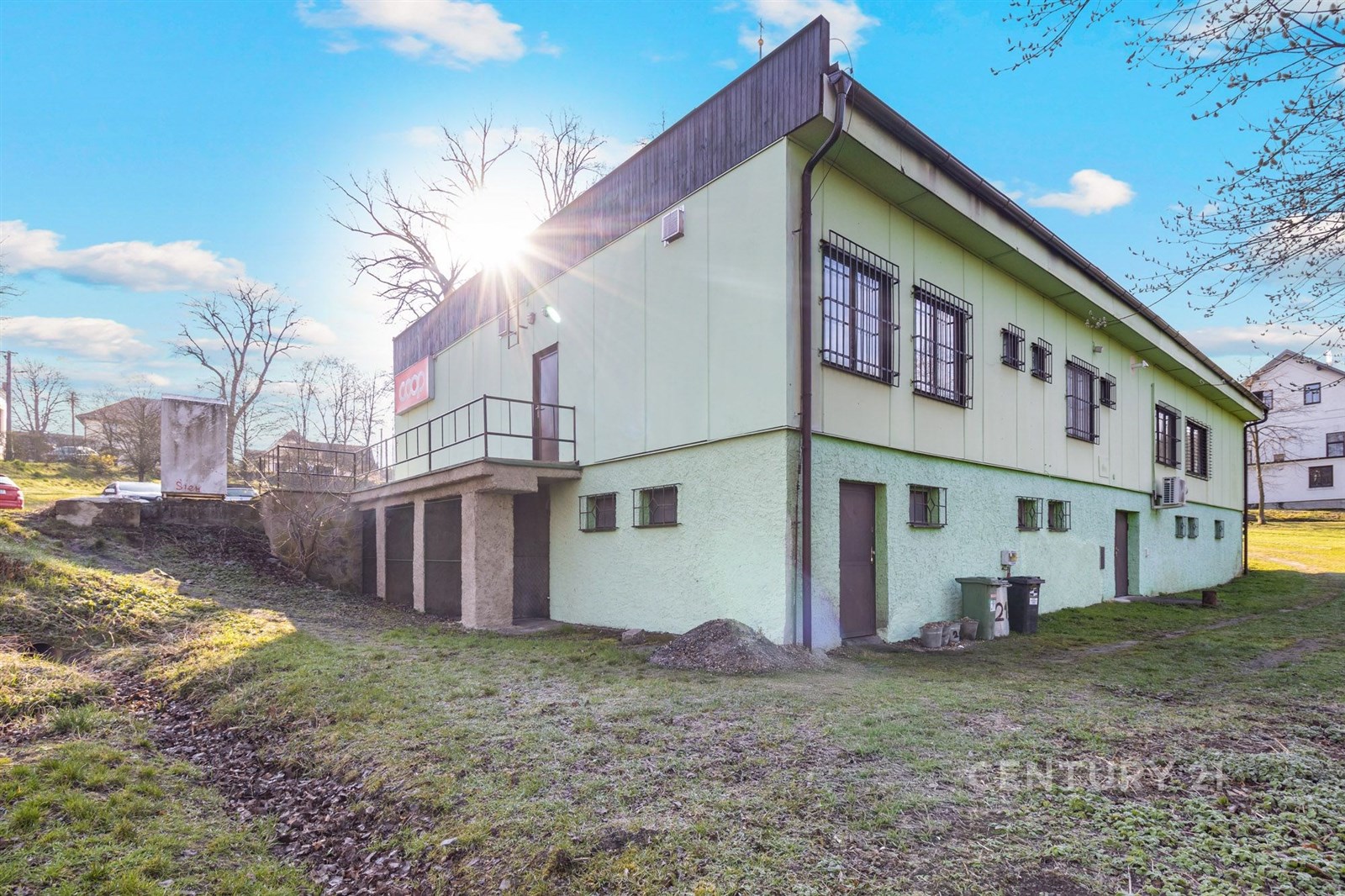 Průmyslová budova s plechovou střechou a velkými okny na travnatém pozemku, vhodná pro komerční využití nebo skladování.