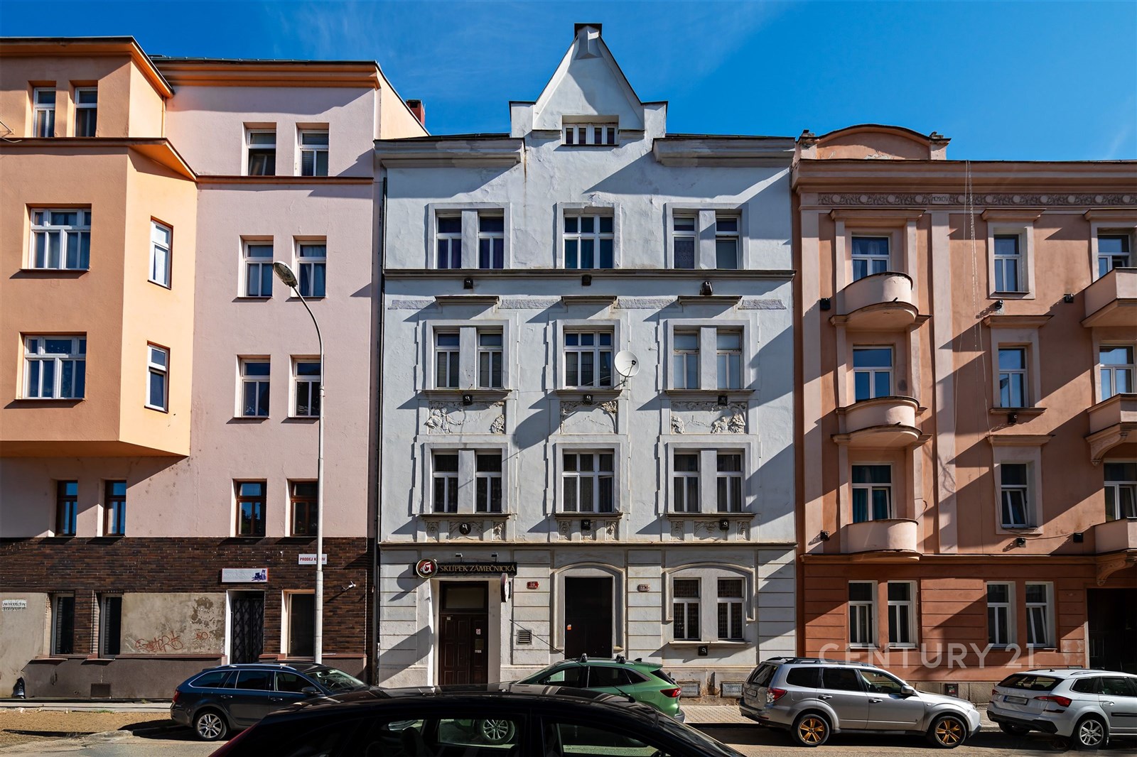 Fasáda historického činžovního domu s původními architektonickými prvky a velkými okny, nacházející se na klidné městské ulici.