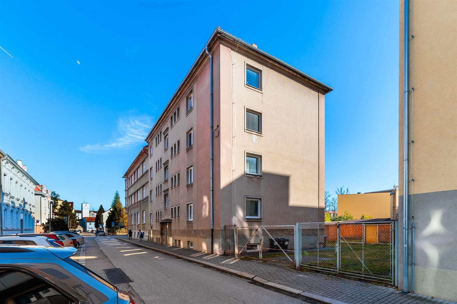 Exteriér bytového domu s klasickou fasádou, nacházející se v klidné rezidenční čtvrti. Budova má čtyři patra a několik oken.