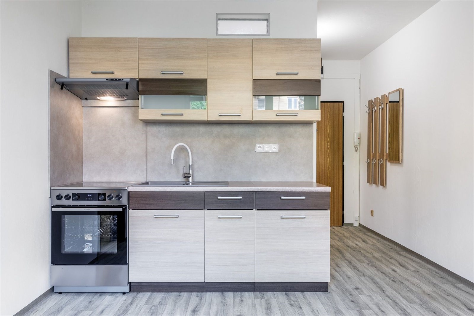 Moderní kuchyň s parketovou podlahou, světlými skříňkami a vestavěnými spotřebiči, nabízí praktický a elegantní prostor pro vaření.