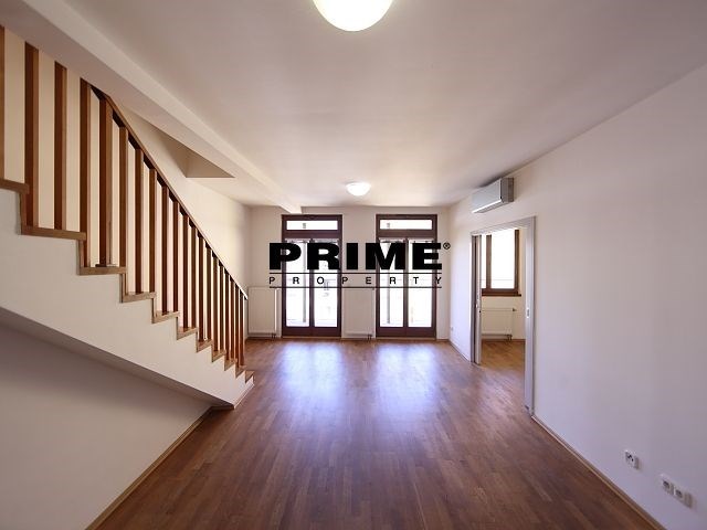 Prostorný obývací pokoj s parketovou podlahou, velkými okny a moderním osvětlením, ideální pro rodinné bydlení.