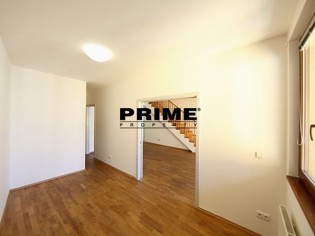 Světlý obývací pokoj s dřevěnou parketovou podlahou, velká okna a čisté bílé stěny, které dodávají moderní a vzdušný pocit prostoru.