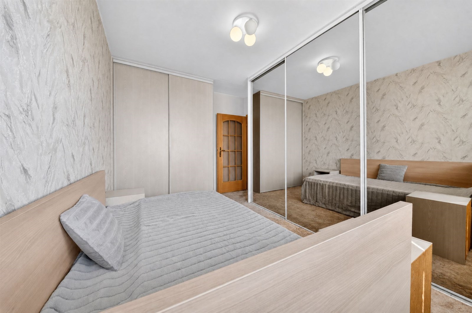 Prostorná ložnice s moderními vestavěnými skříněmi, parketová podlaha, velké zrcadlové dveře, světlé stěny a elegantní osvětlení
