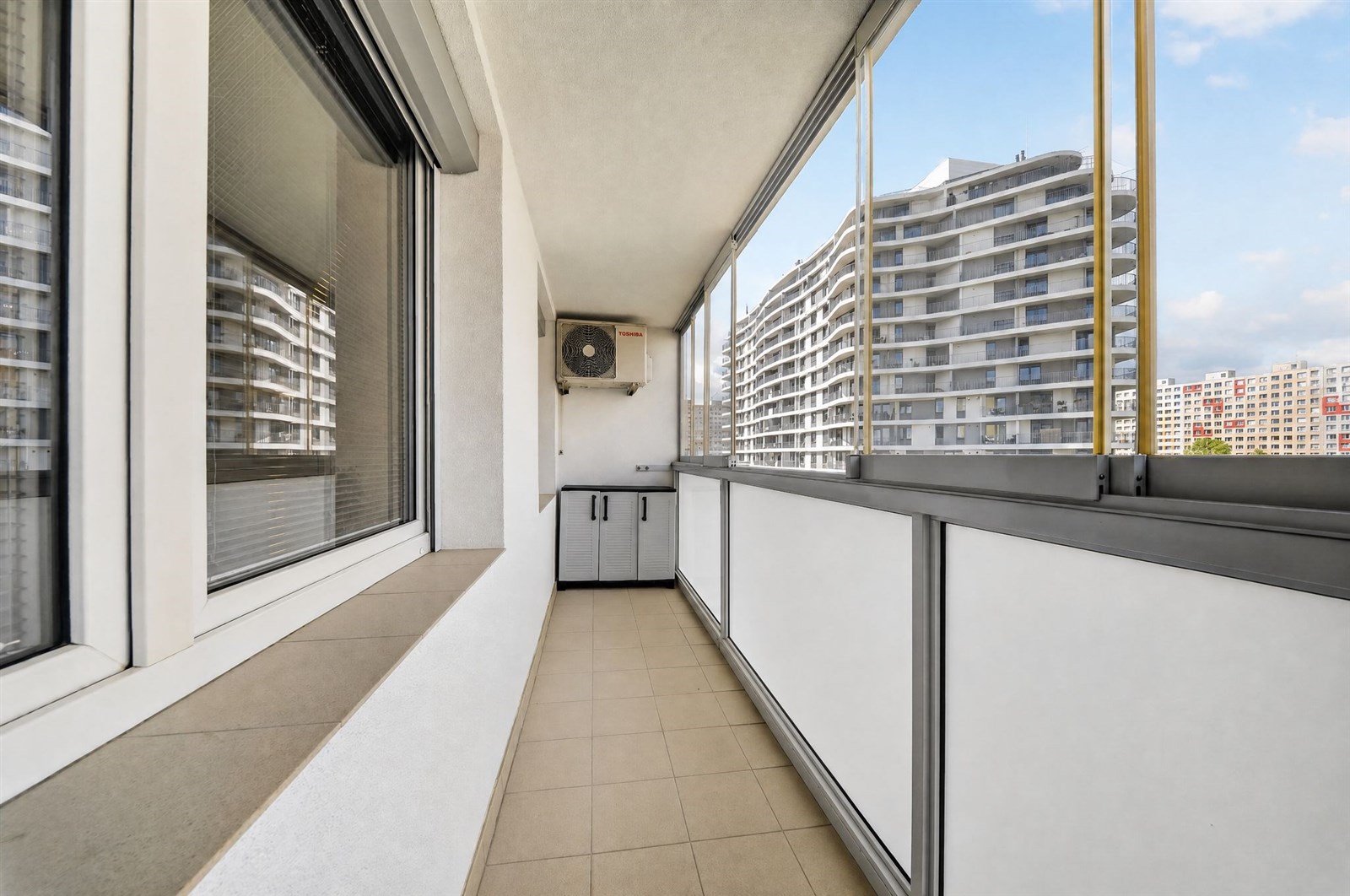 Prostorný balkon s dlažbou a panoramatickým výhledem, moderní design s velkými okny a pečlivě udržovaným zábradlím
