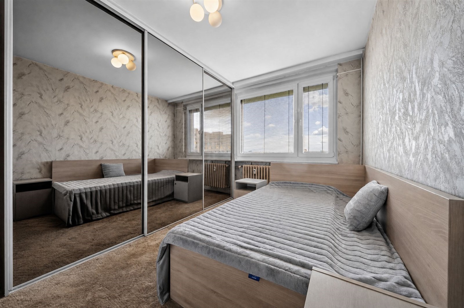 Prostorná ložnice s velkými okny, vestavěnými skříněmi a moderním designem.